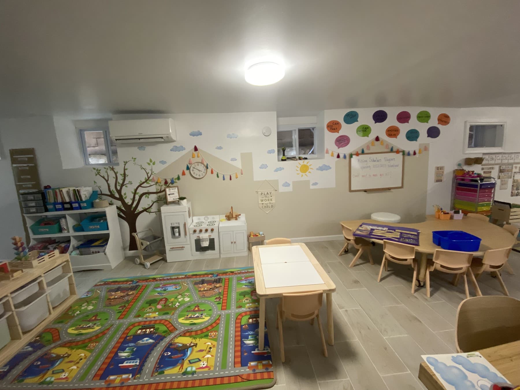 Bright Woodlawn classroom with a play rug, dramatic-play kitchen, bookshelves, and child-sized learning tables