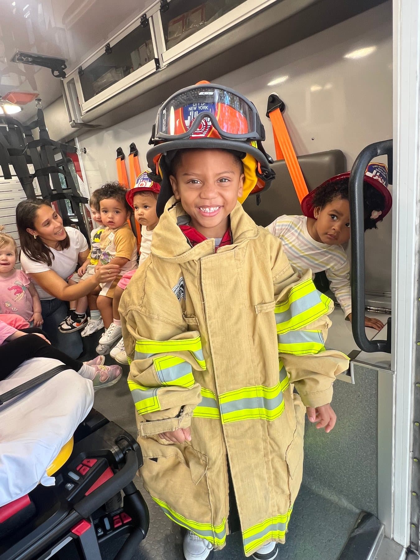 A Rising Scholars child smiling in oversized FDNY firefighter gear during a community learning visit