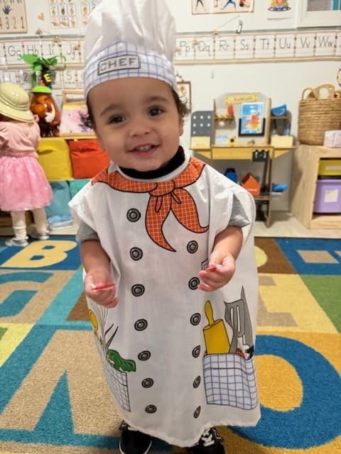 A joyful toddler in a chef costume during dramatic play