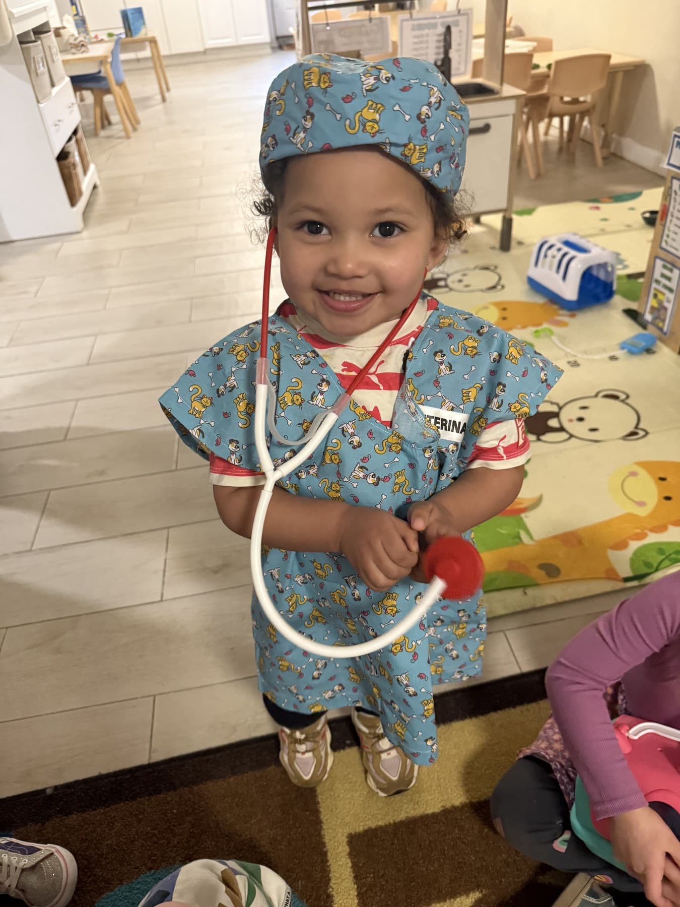 A smiling toddler in a nurse costume holding a toy stethoscope