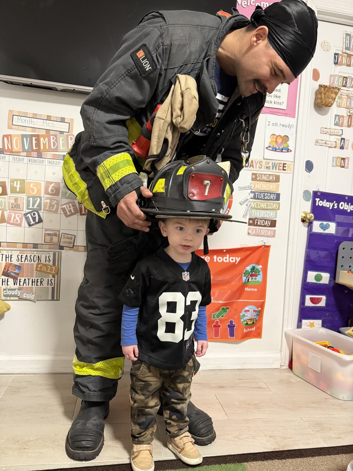 A firefighter placing a helmet on a Rising Scholars toddler during a community visit