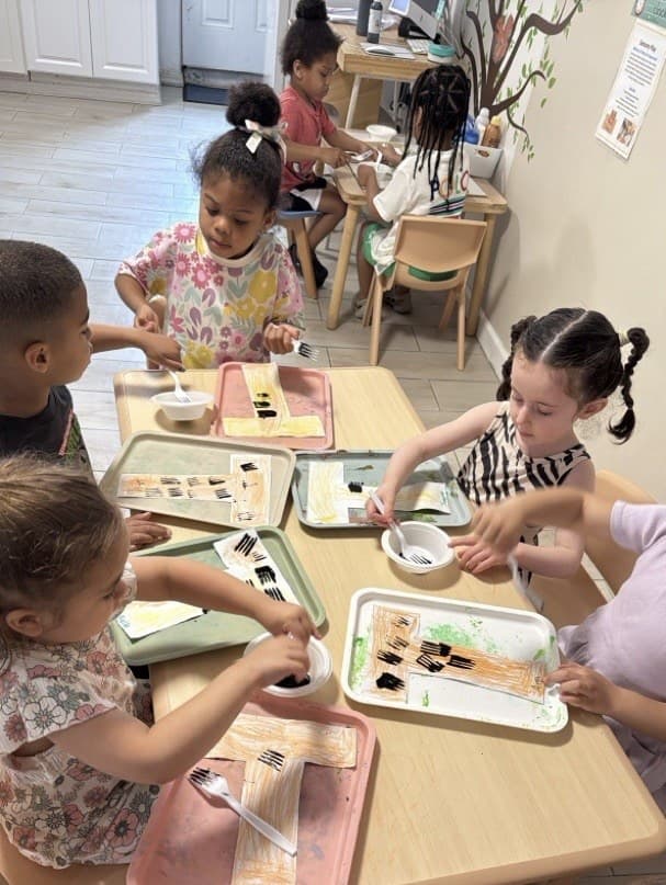 Toddlers creating letter T tiger crafts with paint and forks at the classroom table